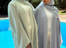 Two women wearing light-colored abayas with lace details by a pool.