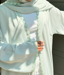 Person wearing a light-colored abaya with floral embroidery, standing against a neutral background.